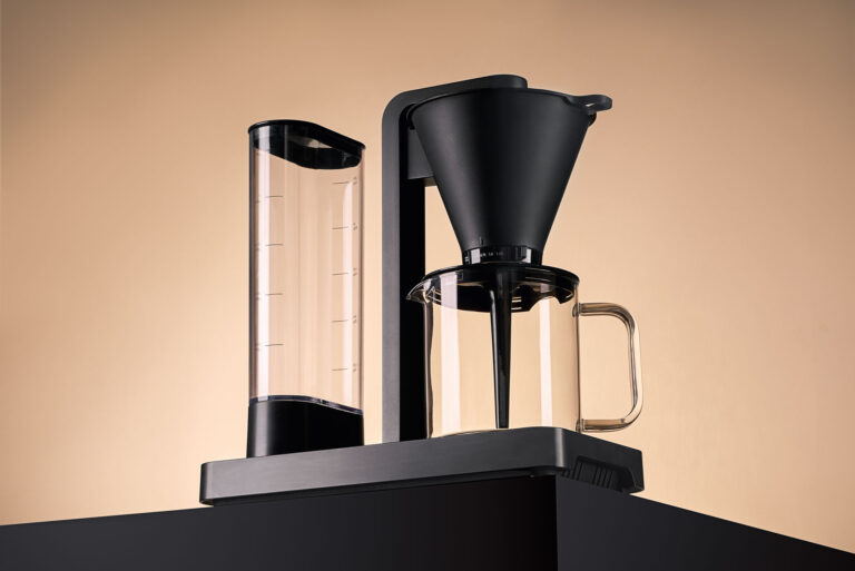 Clean and high-end product photography of a Wilfa coffee machine, utilizing geometric staging and precise studio lighting for commercial advertising, featuring a flawless frontal product portrait showing the complete black coffee maker and its transparent water tank.