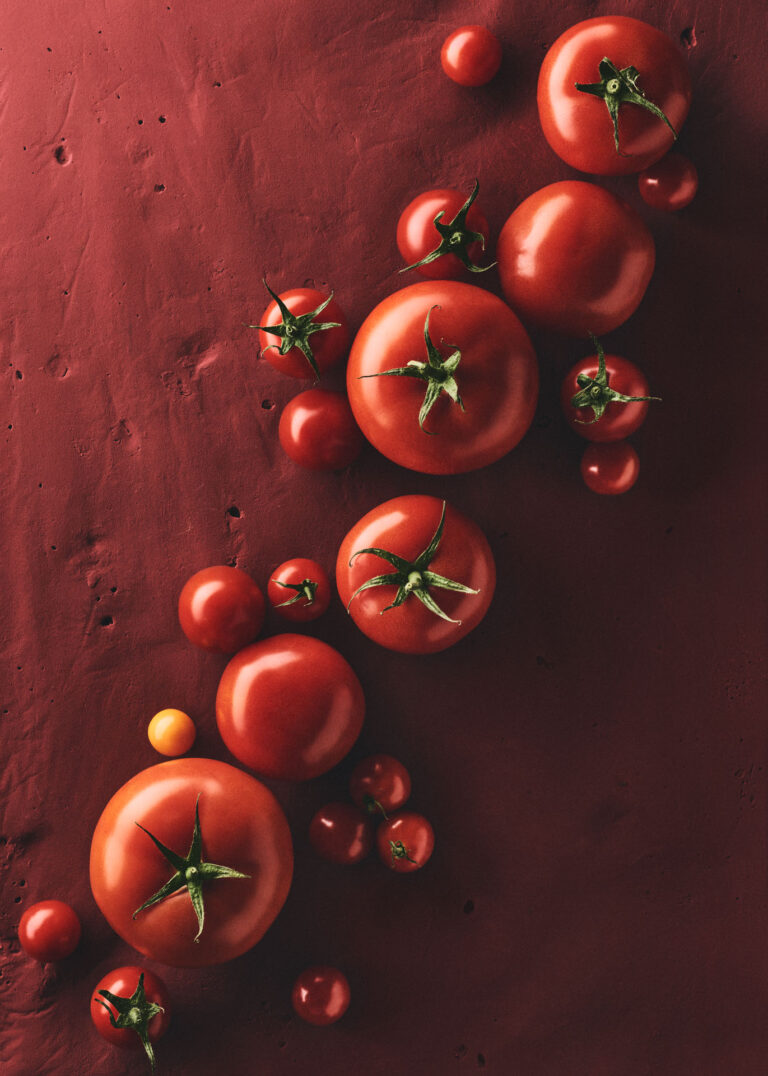 Conceptual and editorial food photography for a design calendar, combining artistic culinary arrangements with structured geometric forms, featuring a vibrant red monochrome composition with various fresh tomatoes on a textured red background.