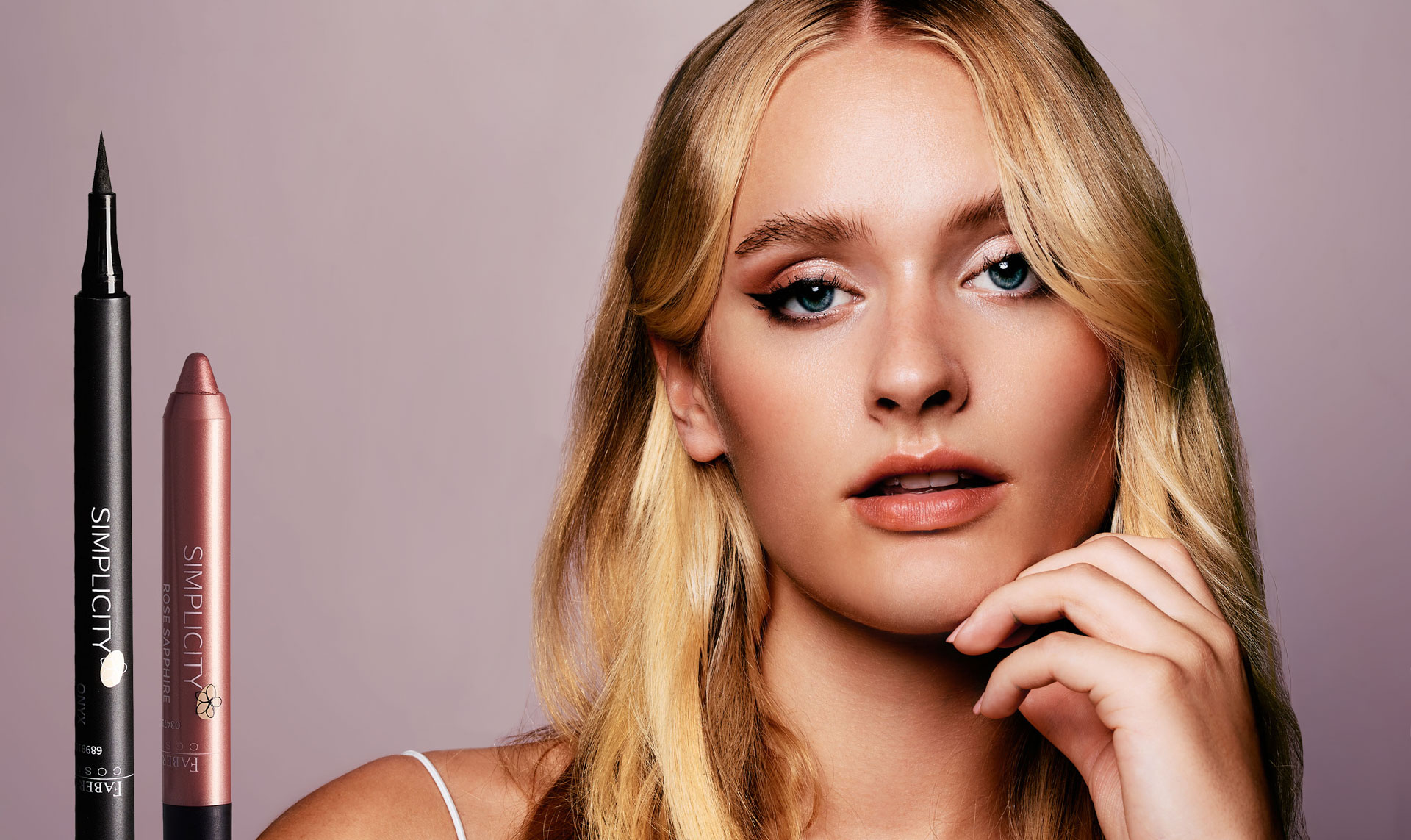 Radiant beauty photography by Lara Zeh emphasizing clean skin texture, pink and brown tones, a glowing look, and expressive eyes, created as a creative concept with Faber-Castell cosmetics, incorporating the sleek cosmetic product design seamlessly into the studio composition next to the model.