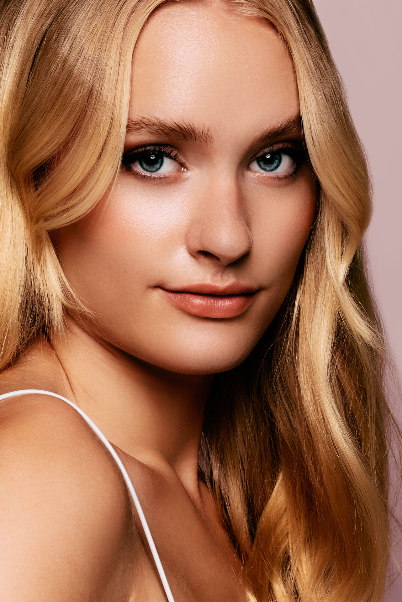Radiant beauty photography by Lara Zeh emphasizing clean skin texture, pink and brown tones, a glowing look, and expressive eyes, created as a creative concept with Faber-Castell cosmetics, featuring a soft, centered studio portrait highlighting the flawless skin finish.