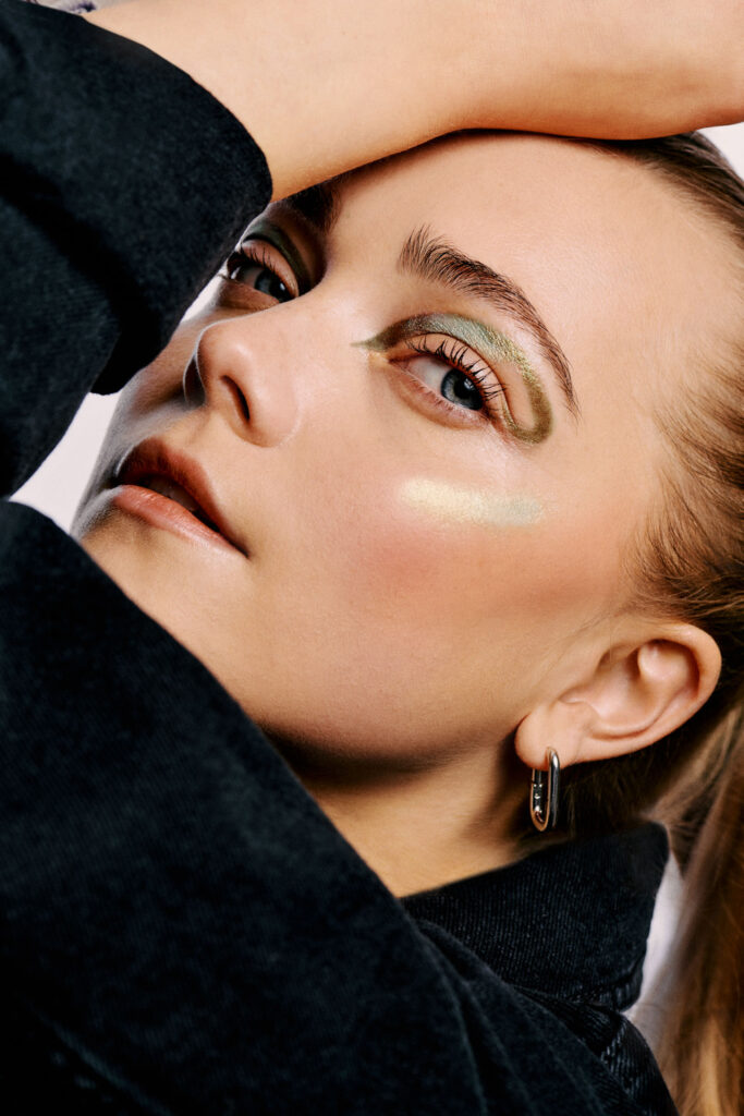High-fashion beauty commercial shot for Faber-Castell Cosmetics featuring multiple models, capturing the sharp metallic reflection and radiance of glitter pigments on the skin under direct lighting, capturing an editorial angle that emphasizes the glowing reflection of high-end cosmetics on the brow bone.