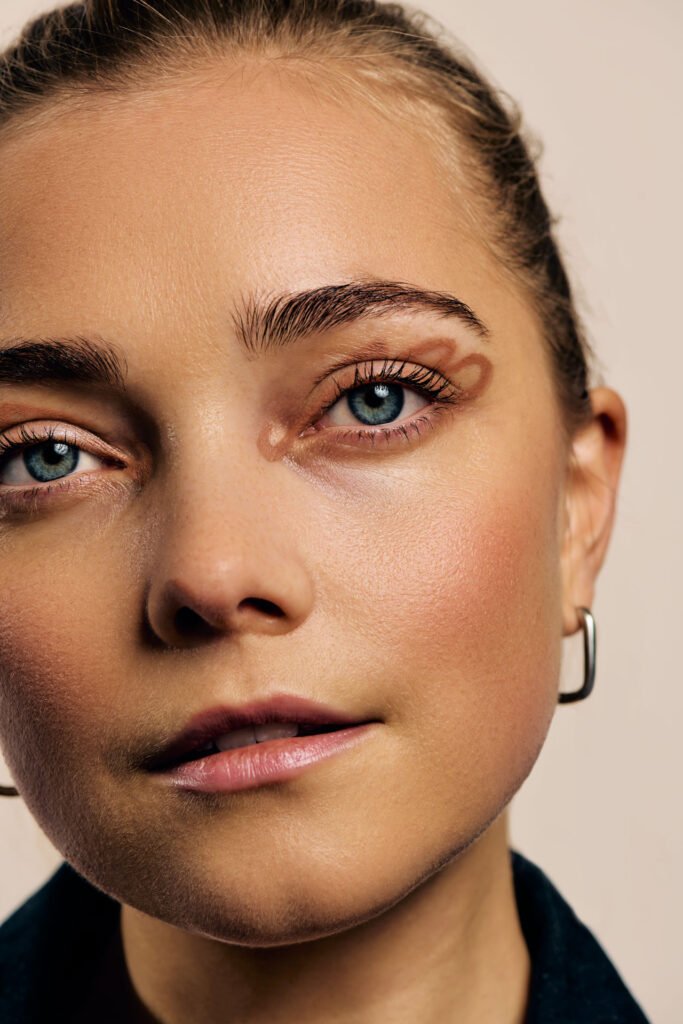 High-fashion beauty commercial shot for Faber-Castell Cosmetics featuring multiple models, capturing the sharp metallic reflection and radiance of glitter pigments on the skin under direct lighting, focusing on a detailed beauty headshot that highlights flawless skin and symmetric graphic eye-art.