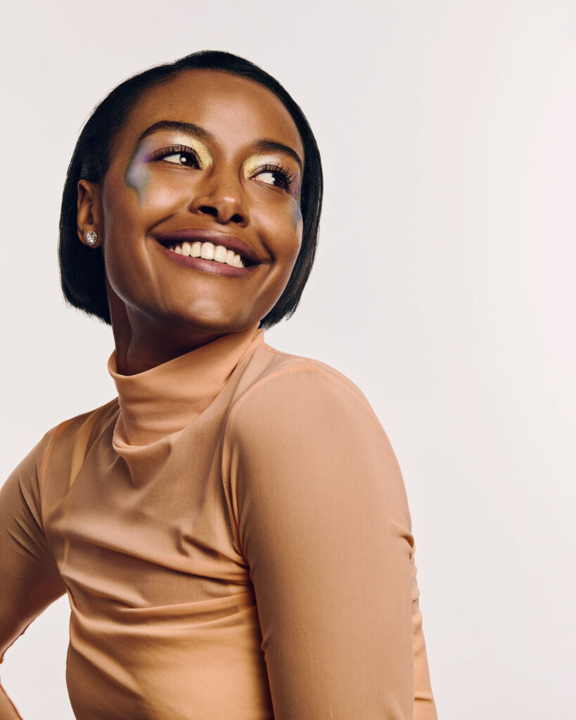 High-fashion beauty commercial shot for Faber-Castell Cosmetics featuring multiple models, capturing the sharp metallic reflection and radiance of glitter pigments on the skin under direct lighting, featuring a joyful studio portrait with dynamic metallic eye make-up art and warm styling.