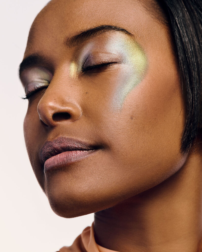 High-fashion beauty commercial shot for Faber-Castell Cosmetics featuring multiple models, capturing the sharp metallic reflection and radiance of glitter pigments on the skin under direct lighting, capturing a serene profile macro shot that emphasizes iridescent, colorful metallic shimmer on the eyelids and temples.