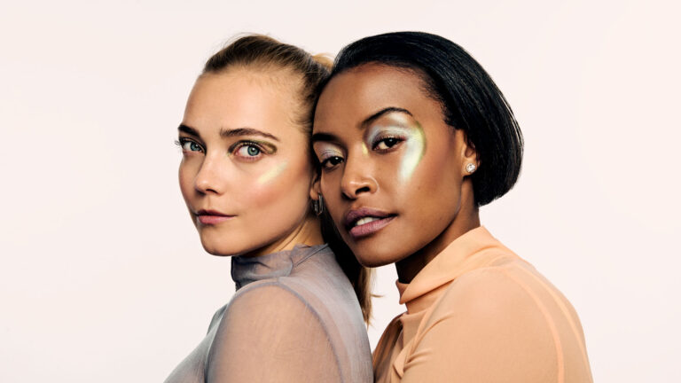 High-fashion beauty commercial shot for Faber-Castell Cosmetics featuring multiple models, capturing the sharp metallic reflection and radiance of glitter pigments on the skin under direct lighting, showcasing a dual model portrait focused on luminous cheekbone highlights and soft textures.