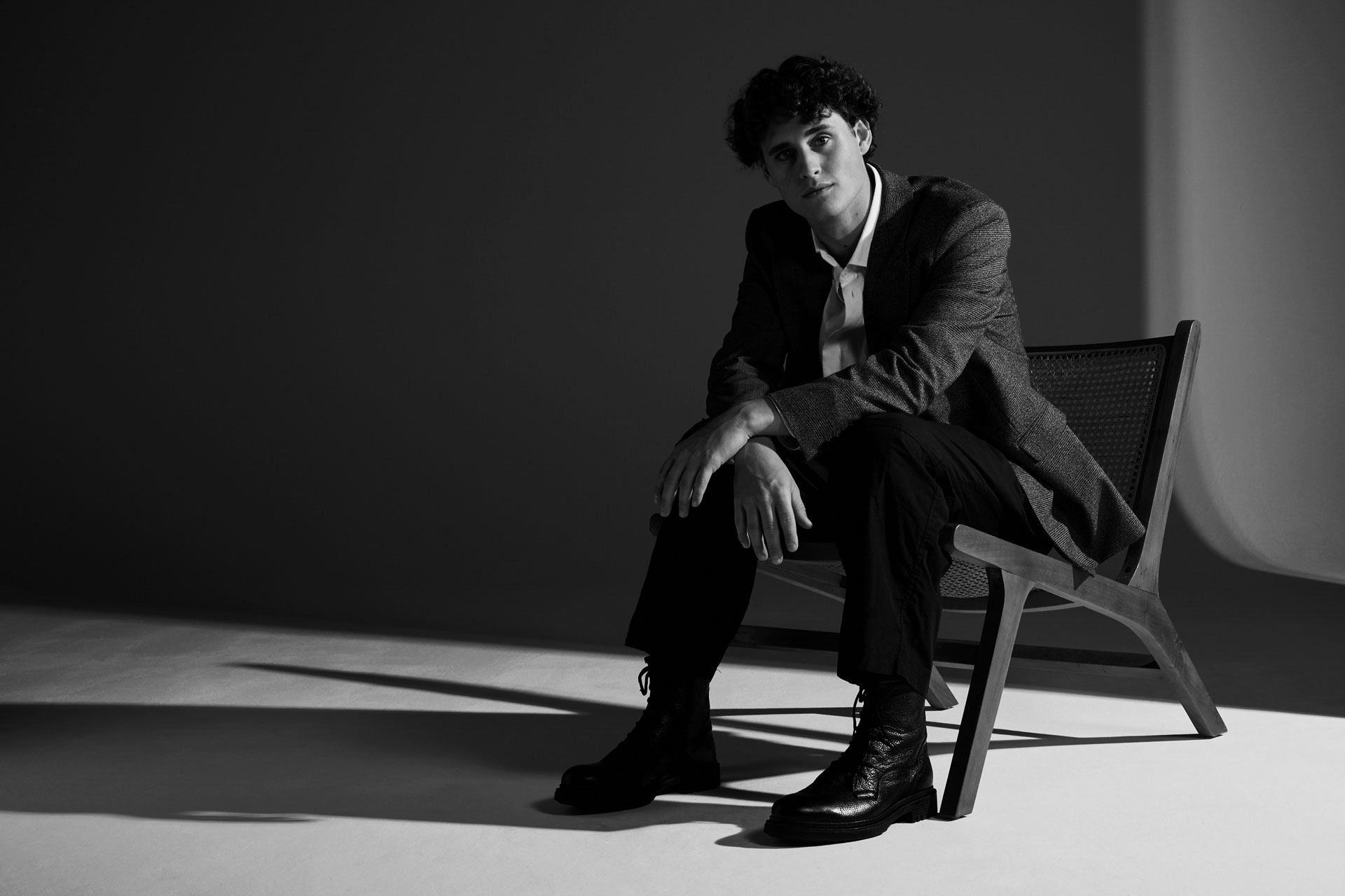 Minimalist studio fashion editorial showcasing a modern brown suit and a flat graphic wooden chair, focusing on structural geometry and high-contrast lighting, concluding the editorial with a full-view black and white studio composition that merges the human silhouette with the design object.