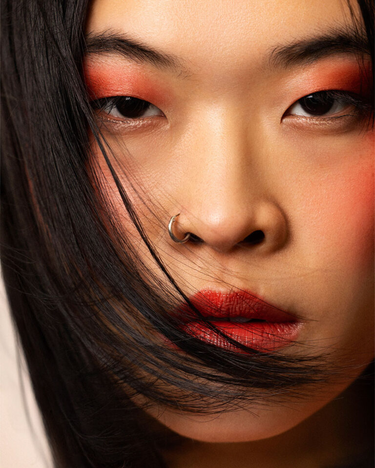 Professional beauty campaign image for Faber-Castell Cosmetics featuring clean studio portraits with diverse models and soft lighting that defines natural contours and warm earth tones, capturing an intense macro beauty shot focused on vibrant red eyeshadow and warm skin blush.