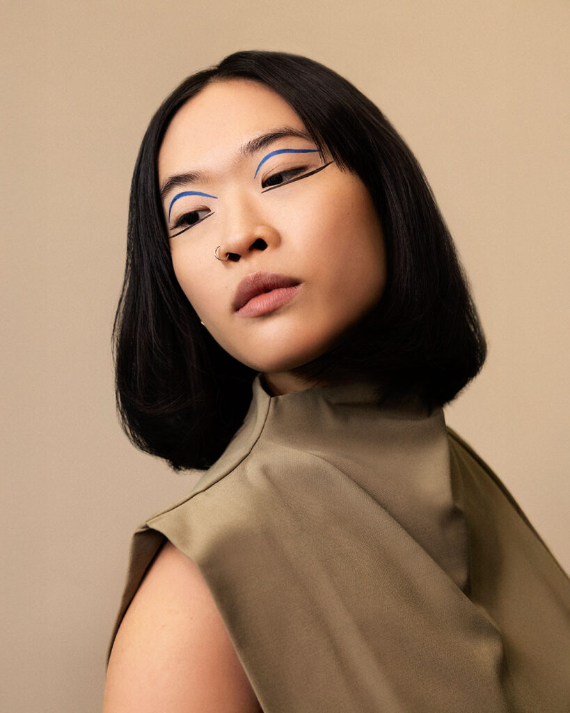Professional beauty campaign image for Faber-Castell Cosmetics featuring clean studio portraits with diverse models and soft lighting that defines natural contours and warm earth tones, featuring a warm-toned studio portrait highlighting an artistic blue and black dual-eyeliner concept.