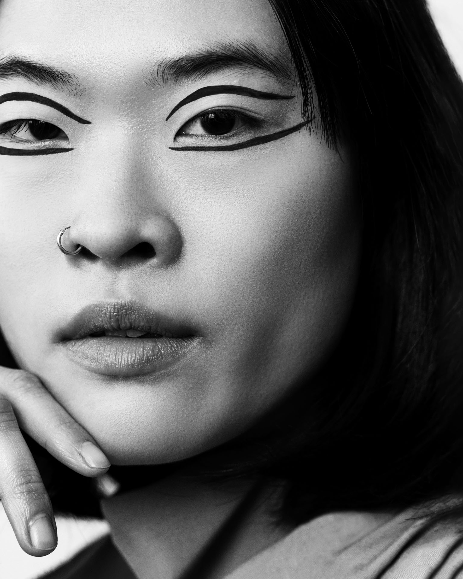 Professional beauty campaign image for Faber-Castell Cosmetics featuring clean studio portraits with diverse models and soft lighting that defines natural contours and warm earth tones, focusing on a black and white close-up with graphic liner art around the eyes.
